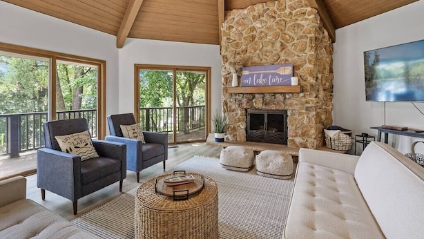 A spacious living room with a stone fireplace, comfortable seating, and large windows overlooking a deck.