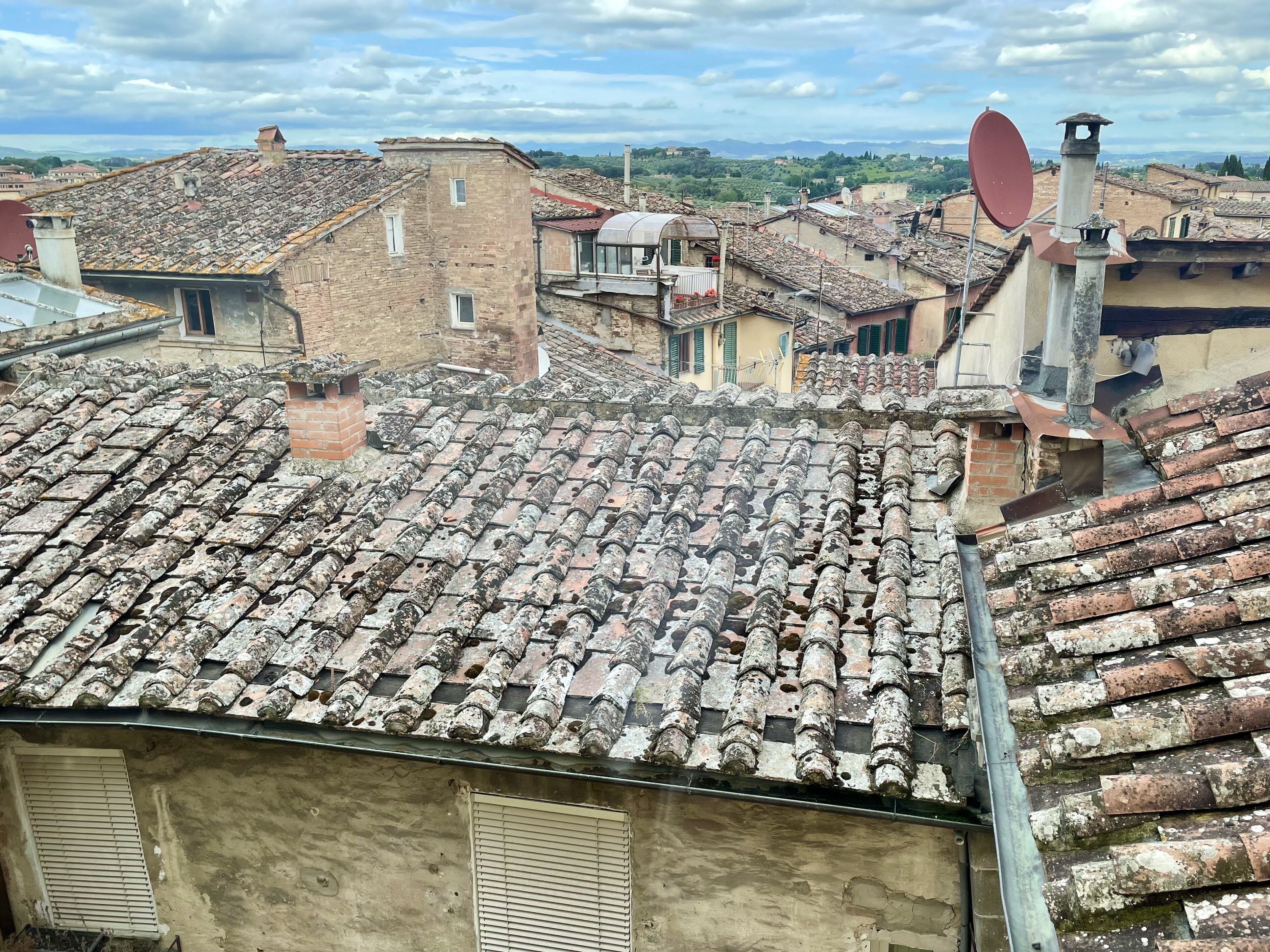 Vue d’une ville avec des toits recouverts de tuiles en terre cuite, une antenne parabolique et un mélange de bâtiments traditionnels et modernes.