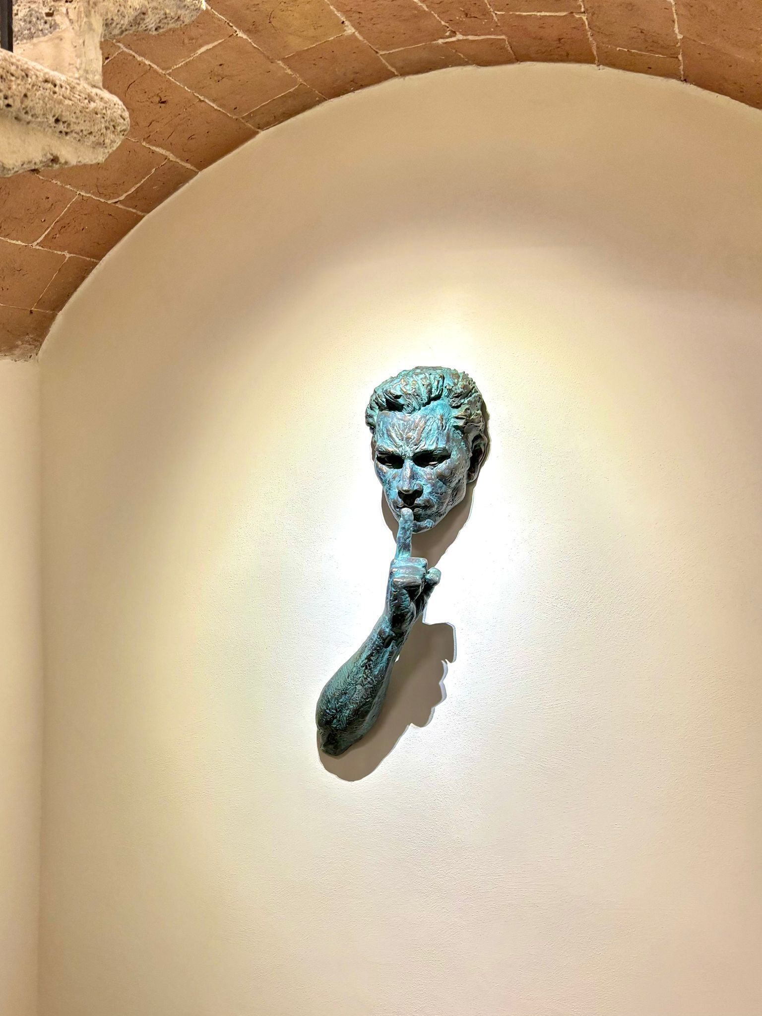 A bronze bust mounted on a wall with a brick arch above it.