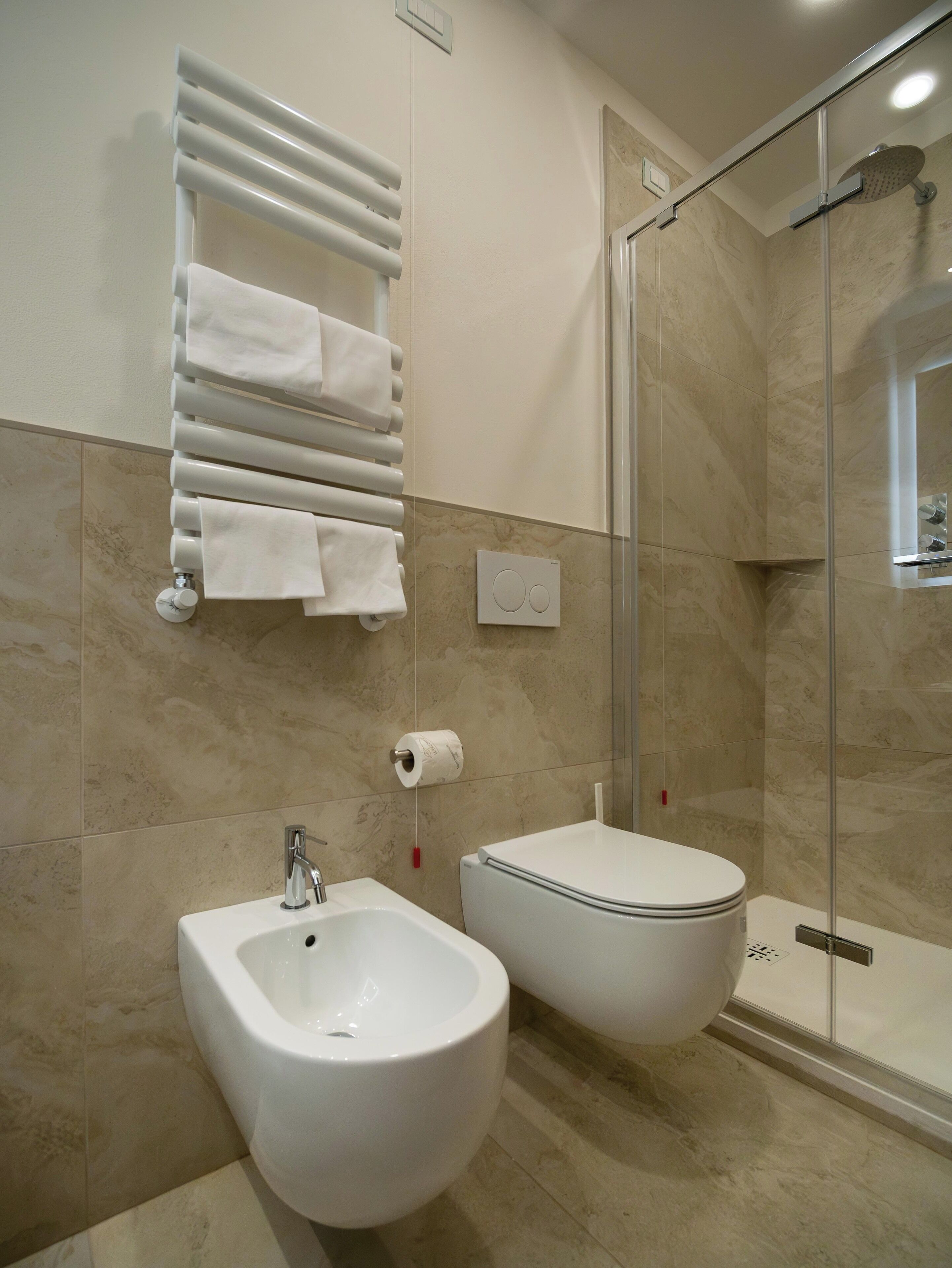 Un baño moderno con bidé, ducha con mampara de vidrio y toallero con múltiples toallas.