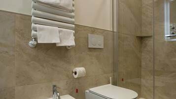 Un baño moderno con bidé, ducha con mampara de vidrio y toallero con múltiples toallas.