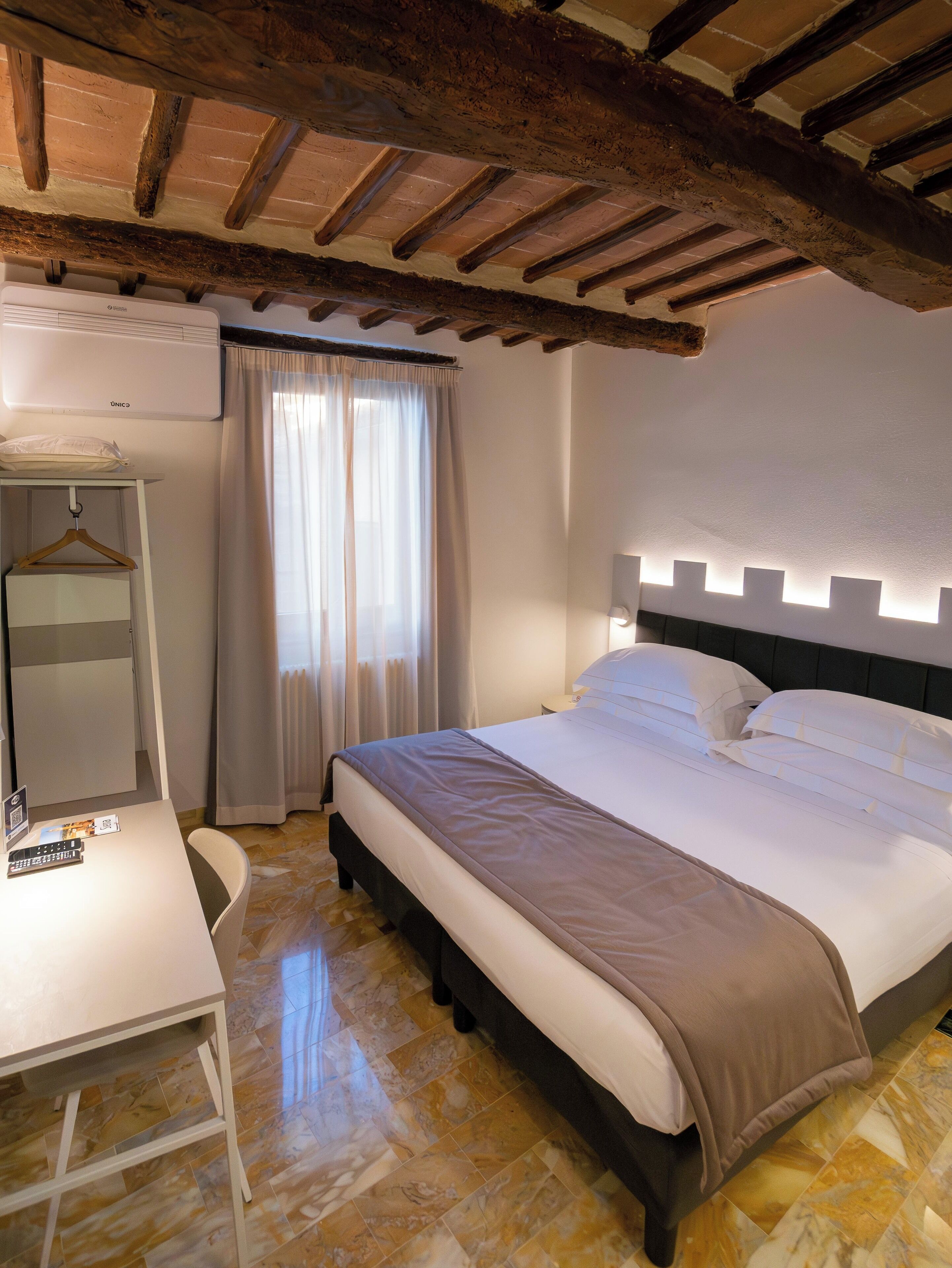 A bedroom with a bed, a desk, a chair, a wardrobe, and a window with curtains.