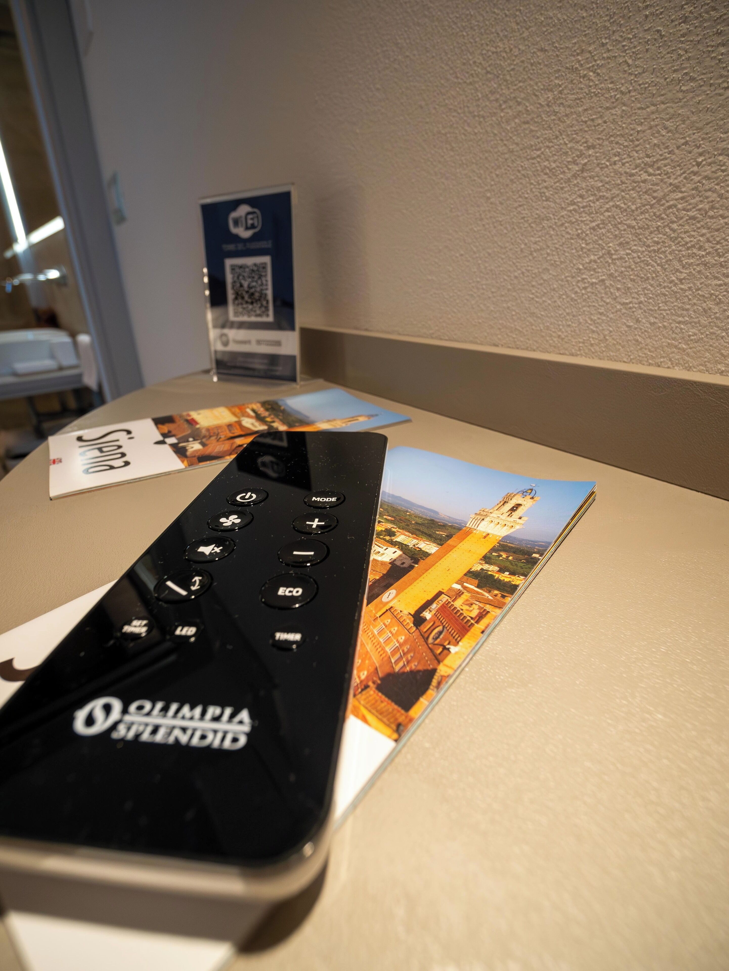 A remote control on a table with a brochure and a QR code.