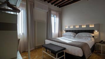 A bedroom with a bed, bedside tables, a bench, a radiator, and a window with curtains.