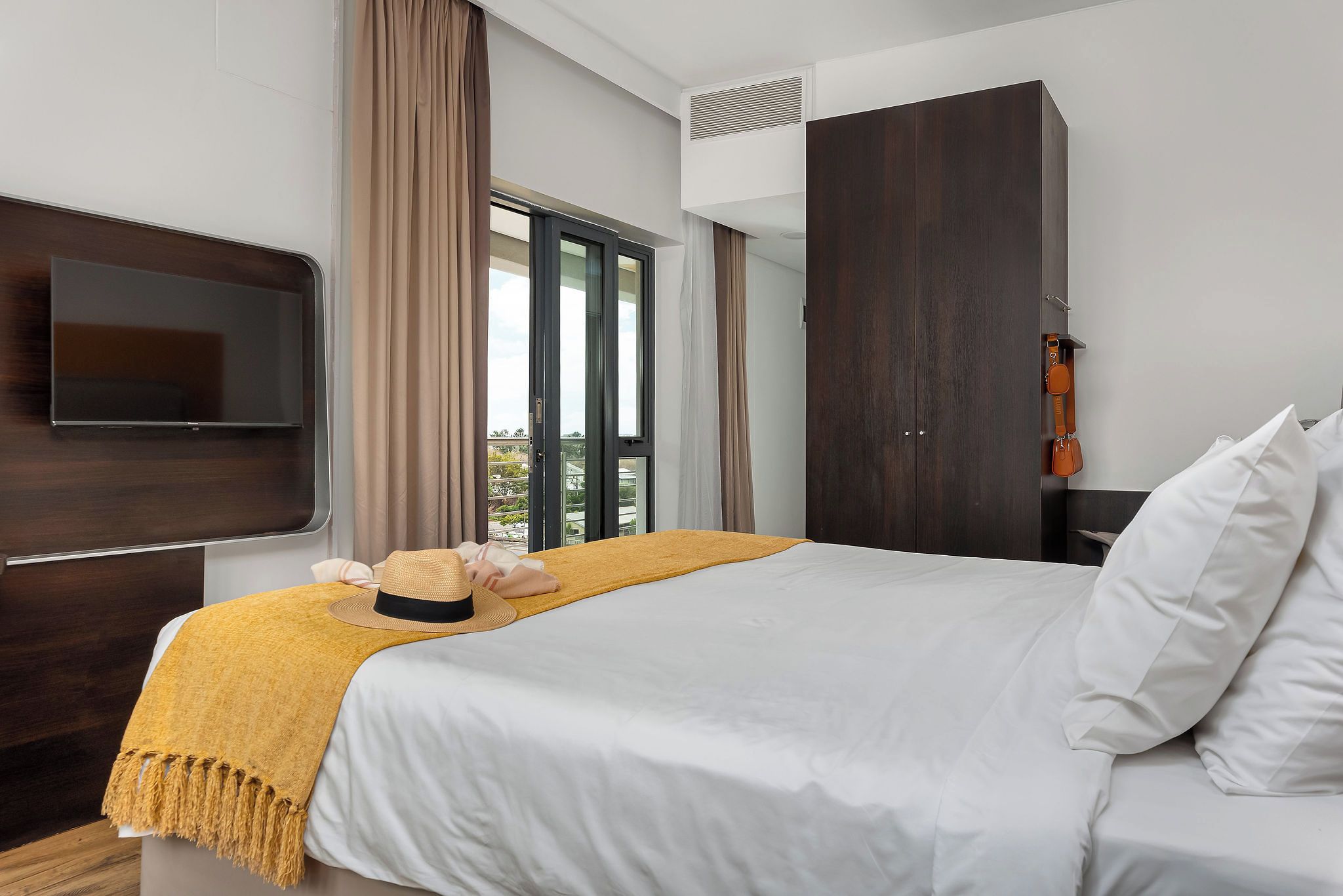 A hotel room with a bed, a TV, a wardrobe, and a view of the outdoors.