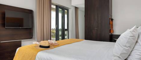 A hotel room with a bed, a TV, a wardrobe, and a view of the outdoors.
