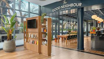 Interior de una cafetería moderna con estantería de madera, zona de estar y grandes ventanales.