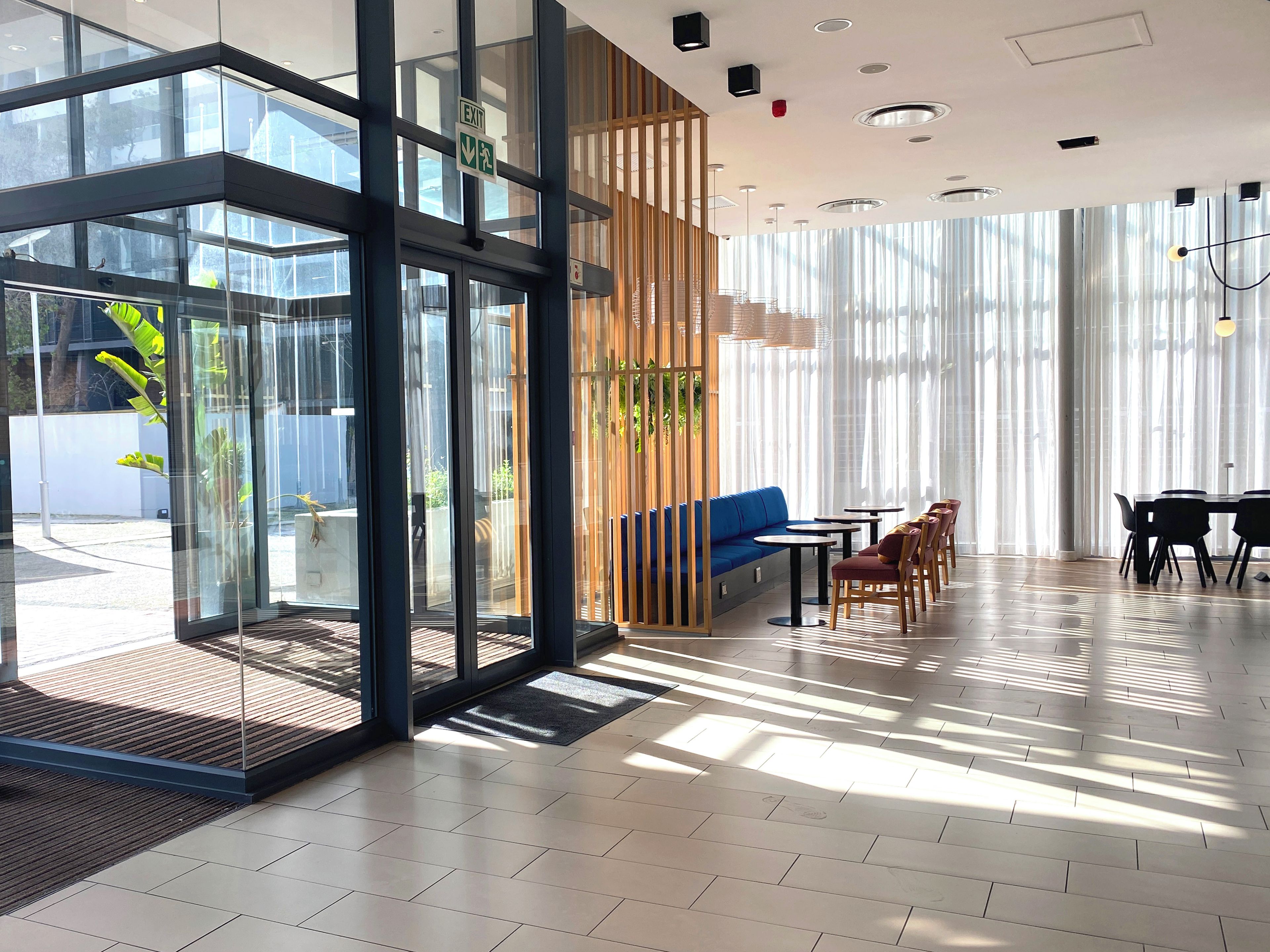 A modern interior with glass doors, a seating area with tables, and a view through large windows.