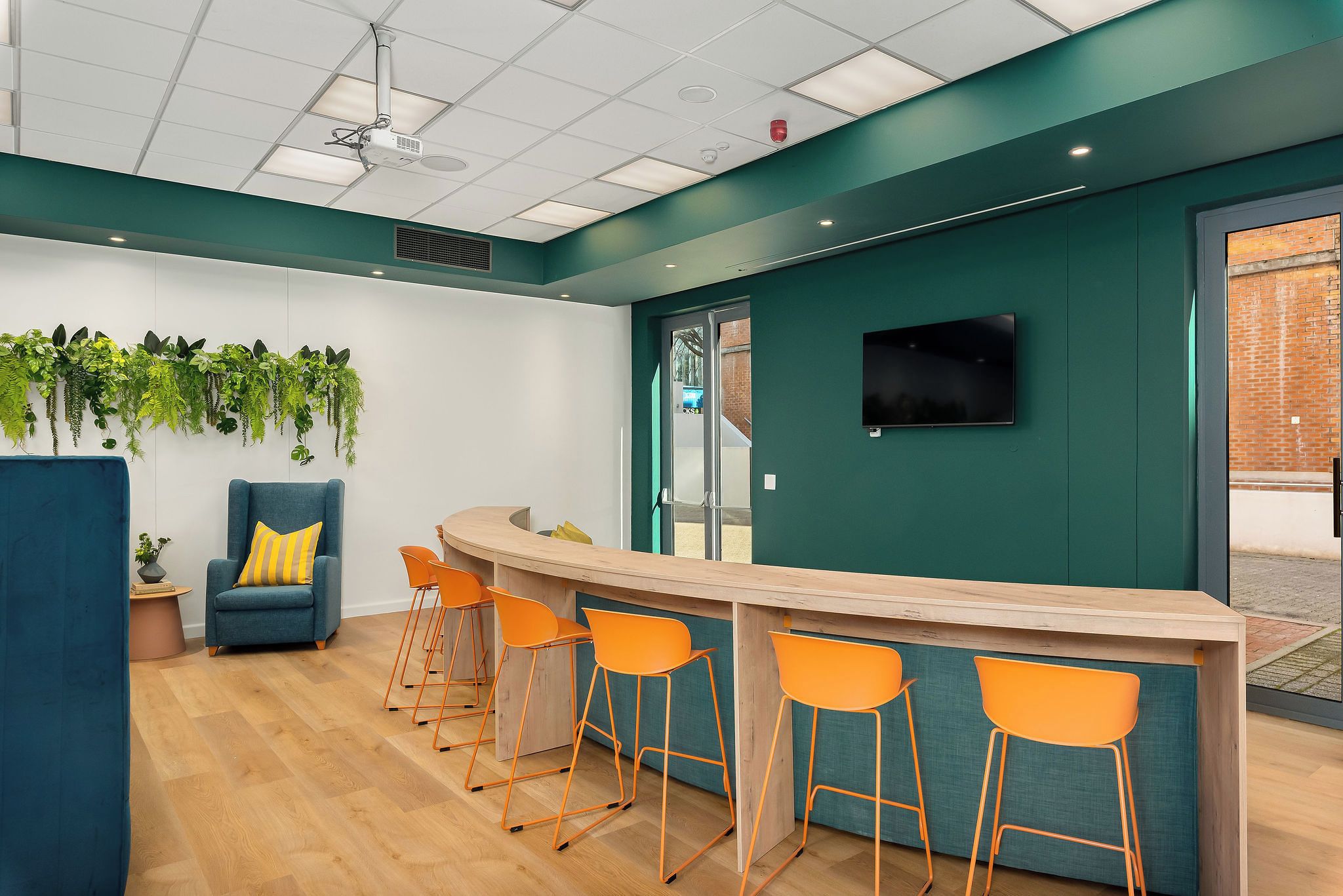 A modern bar area with a counter and orange chairs, a blue sofa with a yellow pillow, and a wall-mounted TV.
