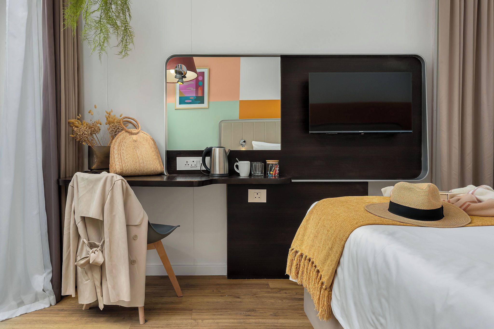 A hotel room with a bed, a desk with a TV, a chair, a coffee maker, and a decorative wall.