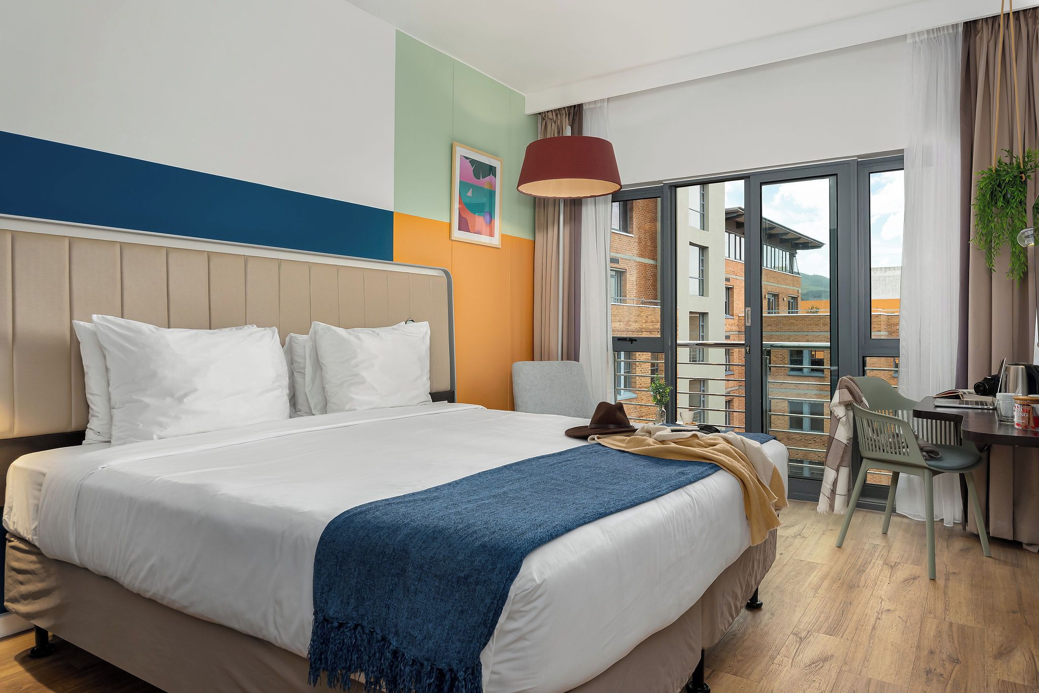A hotel room with a large bed, a desk, and a view of the city through the window.