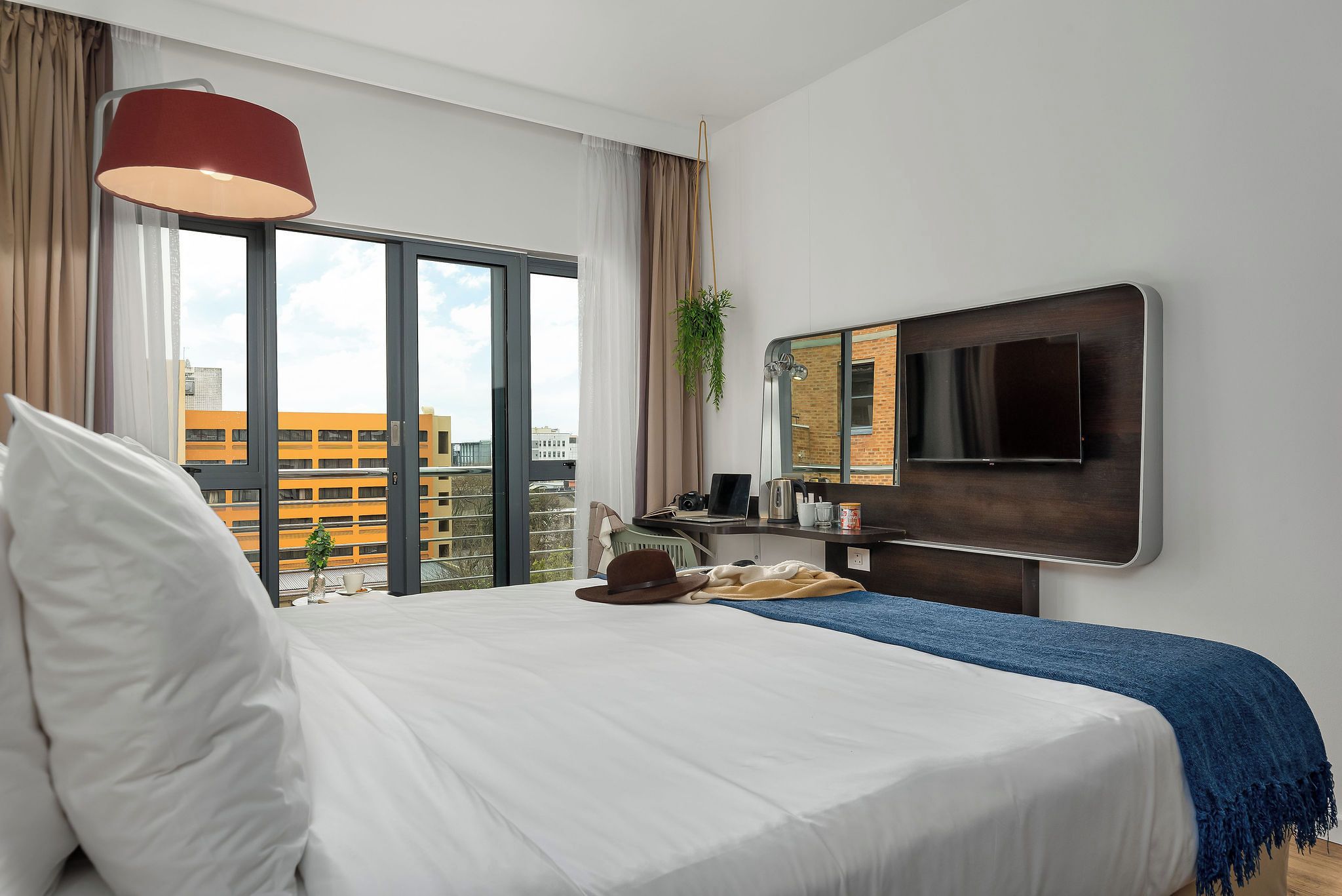 Habitación de hotel con una cama grande, un televisor montado en la pared y vistas de la ciudad a través de la ventana.