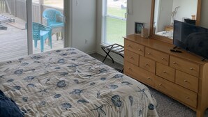 Une chambre à coucher comprenant un lit, une commode, une télévision et un balcon avec des chaises.