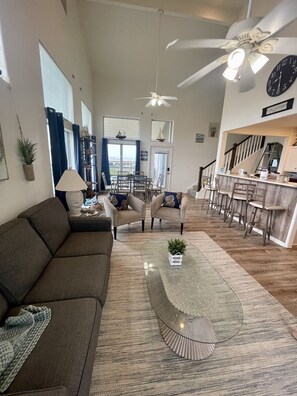 A spacious living room with a large sofa, a coffee table, and a dining area with chairs and a table.