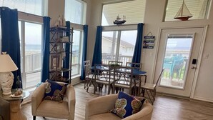 Un vaste salon doté d’une grande fenêtre donnant sur un balcon, un coin repas avec des meubles en bois et un ventilateur de plafond.