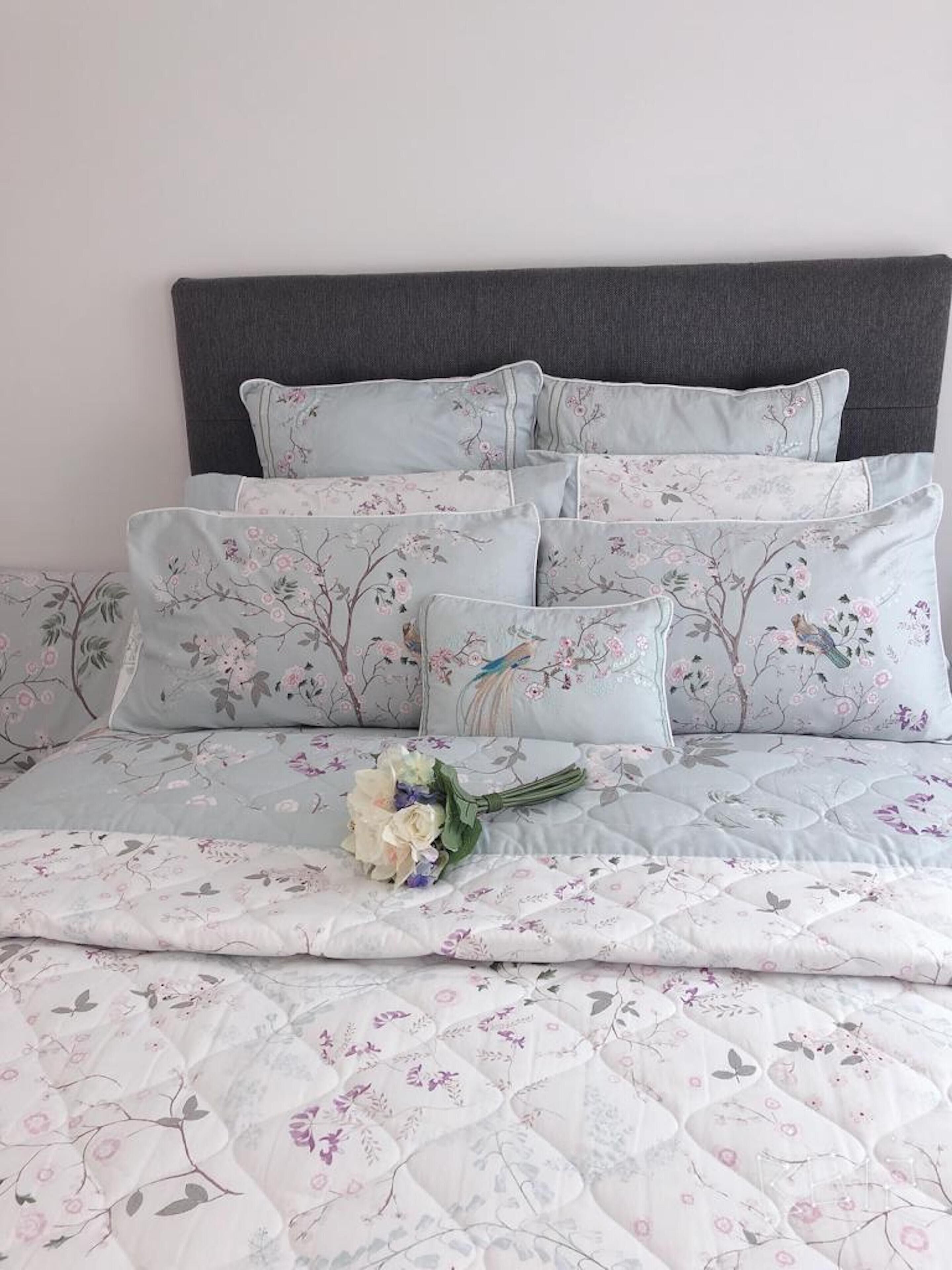 A neatly made bed with floral-patterned bedding and pillows, a bouquet of flowers, and a dark headboard.