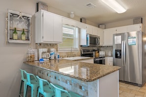 Una cocina con alacenas blancas, encimera de granito, refrigerador de acero inoxidable y microondas integrado.