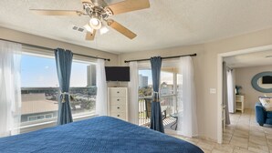 Ein Schlafzimmer mit einem großen Bett, einem Deckenventilator, einem Fernseher und einem Balkon mit Blick auf die Stadt.