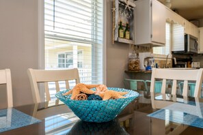 Una mesa de comedor con un tazón azul de mosaicos que contiene estrellas de mar, sillas blancas y una cocina al fondo.