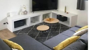 Een moderne woonkamer met een flatscreen televisie, een bank en twee ronde salontafels.