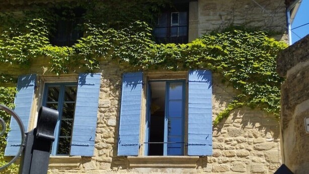 Ein Steinhäuschen mit blauen Fensterläden, einem sichtbaren Fenster und einem kleinen Balkon mit Pflanzen.