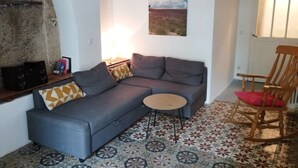 Ein Wohnzimmer mit grauem Sofa, einem kleinen runden Tisch, einem Holzschaukelstuhl und einem Boden mit Musterfliesen.