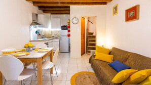 A compact living space with a dining area, kitchen, and a sofa with yellow and blue cushions. - L'Observance - Au cœur du centre historique (Arles)