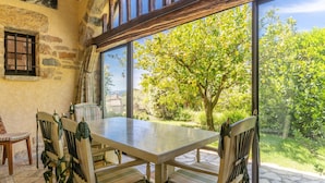 A dining area with a table and chairs, a stone wall, and a large window with a view of greenery and a tree.