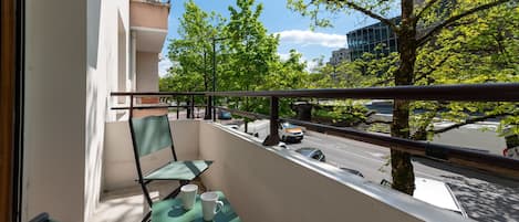 A balcony with a table and chairs, a railing, and a view of a street with cars and trees.