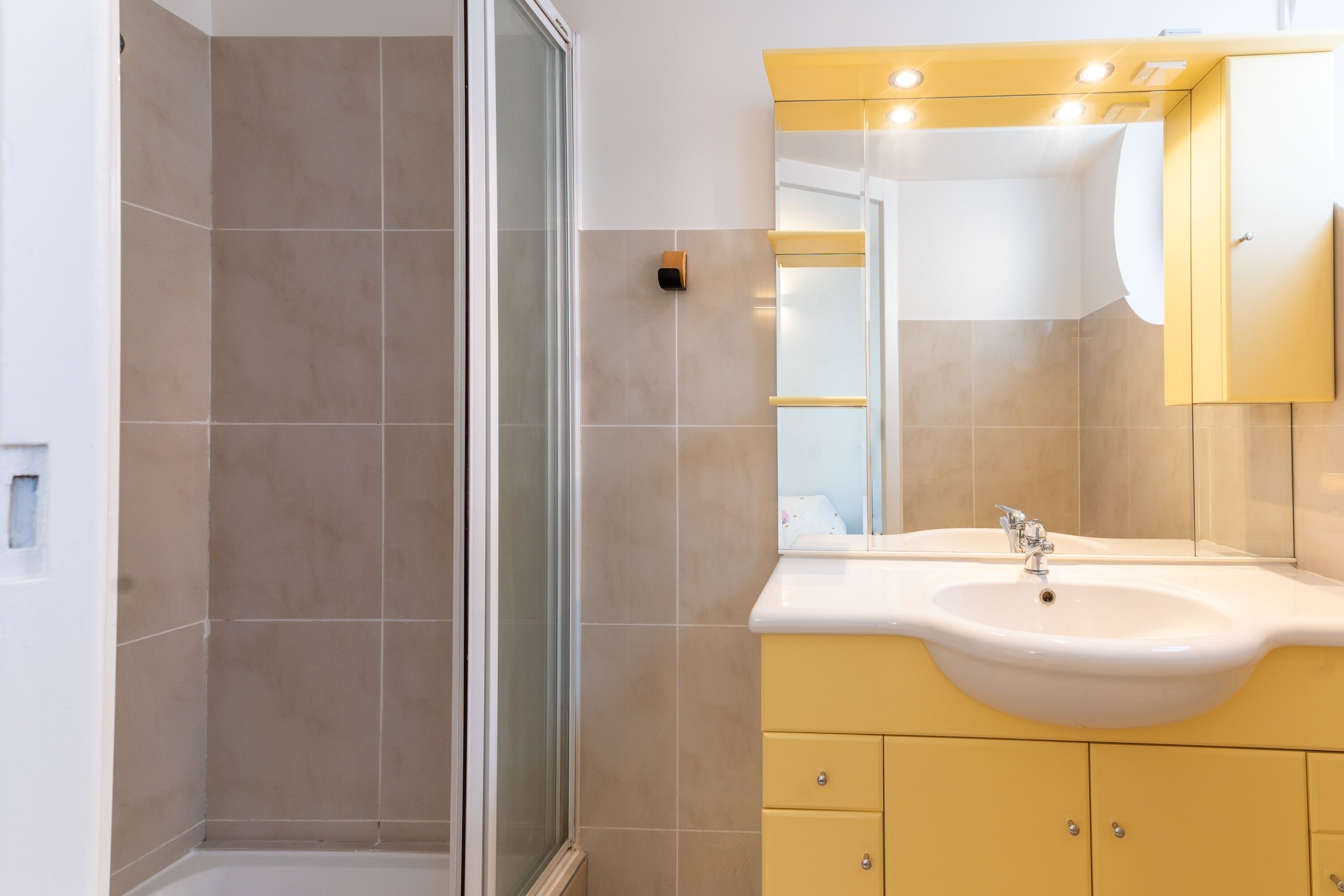 A bathroom with a shower, a sink, and yellow cabinets.