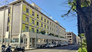 A modern building with a flat facade, large windows, and a parking lot with cars and motorcycles. - Jolly Charme Suite (Messina)