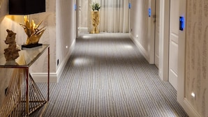 A hotel hallway with a striped carpet, wooden ceiling, and a reception desk with a TV and decorative items. - Jolly Charme Suite (Messina)