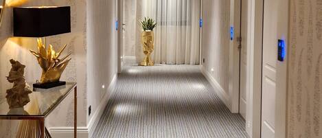 A hotel hallway with a striped carpet, wooden ceiling, and a reception desk with a TV and decorative items.