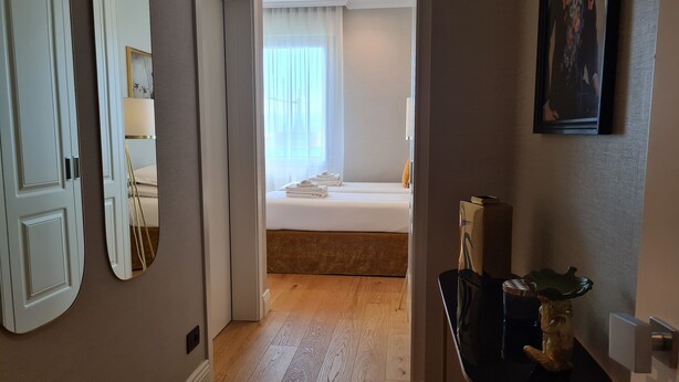 A hotel room with a wooden floor, a bed with white linens, a bedside table with a lamp, and a large mirror on the wall. - Jolly Charme Suite (Messina)
