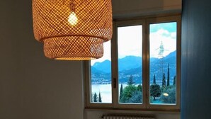 A bedroom with a bed, a window with a view of mountains, and a hanging light fixture. - Renovated, amazing lake view (Perledo)