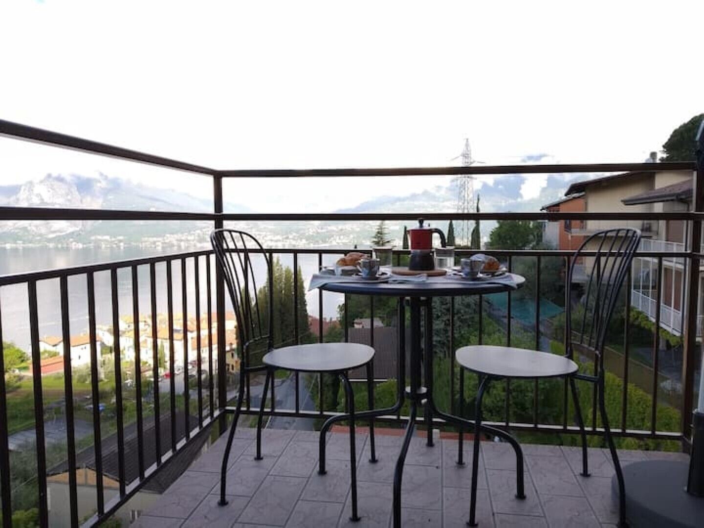 Ein Balkon mit zwei Stühlen und einem kleinen Tisch mit Blick auf ein Gewässer und Berge.