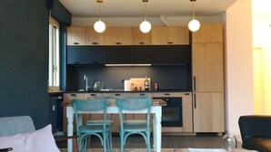 A modern kitchen with wooden cabinets, a dining area with teal chairs, and a terrazzo floor. - Renovated, amazing lake view (Perledo)