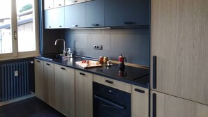 A modern kitchen with wooden cabinets, a black countertop, and a window providing natural light. - Renovated, amazing lake view (Perledo)