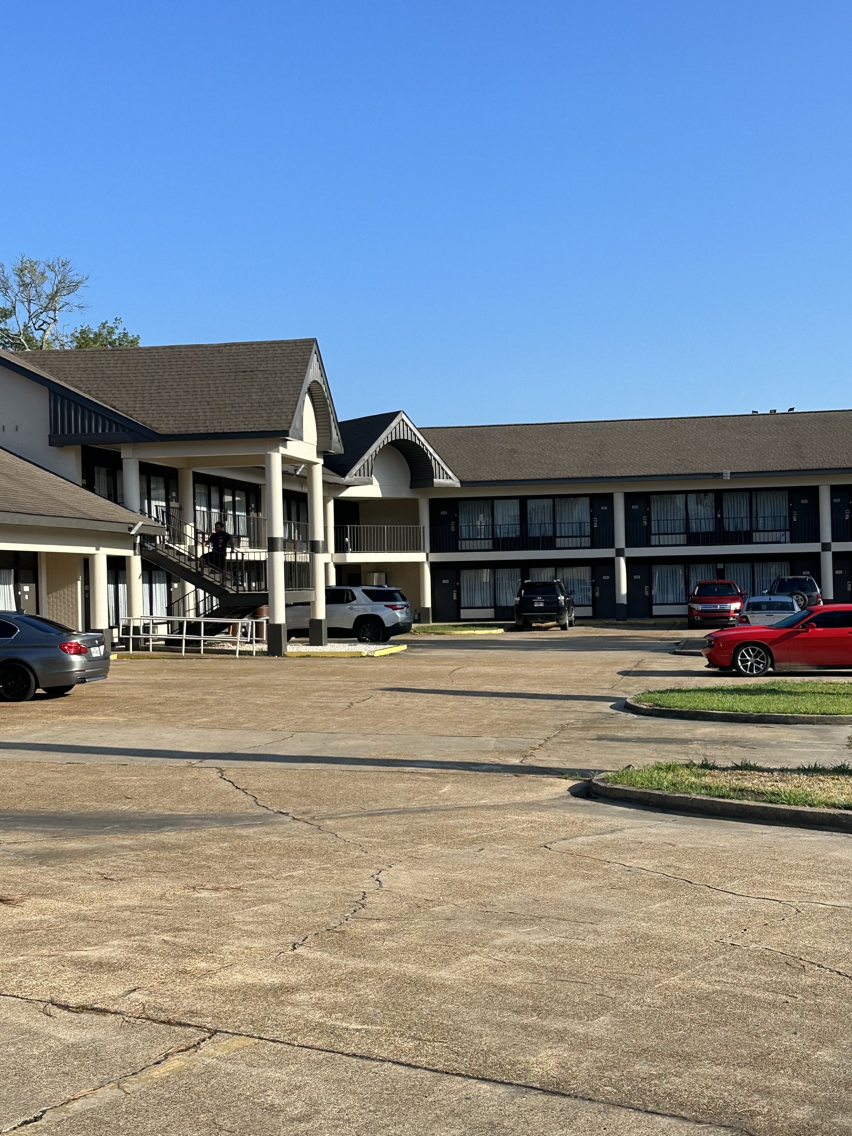Un motel con una escalera central, varios espacios de estacionamiento y un área exterior techada.