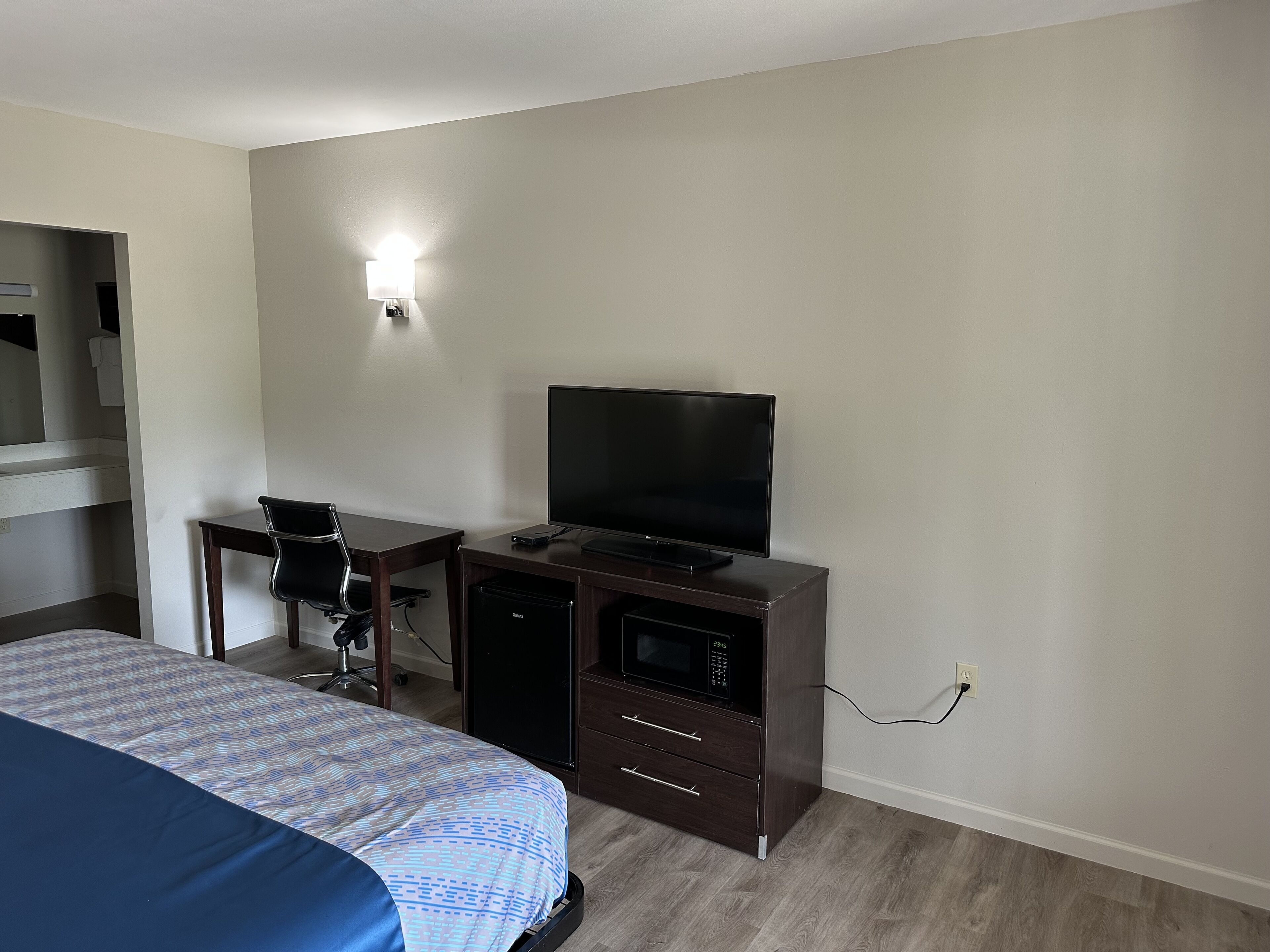 Une chambre d’hôtel comprenant un lit, un bureau avec un ordinateur et une télévision, une chaise et une petite kitchenette.