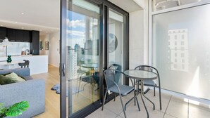 A modern apartment with a glass sliding door leading to a balcony, a dining area with a round table and chairs, and a kitchen with dark cabinets.