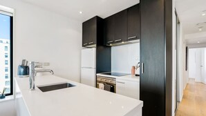 A modern kitchen with white countertops, dark cabinetry, a built-in oven, and a stainless steel sink.