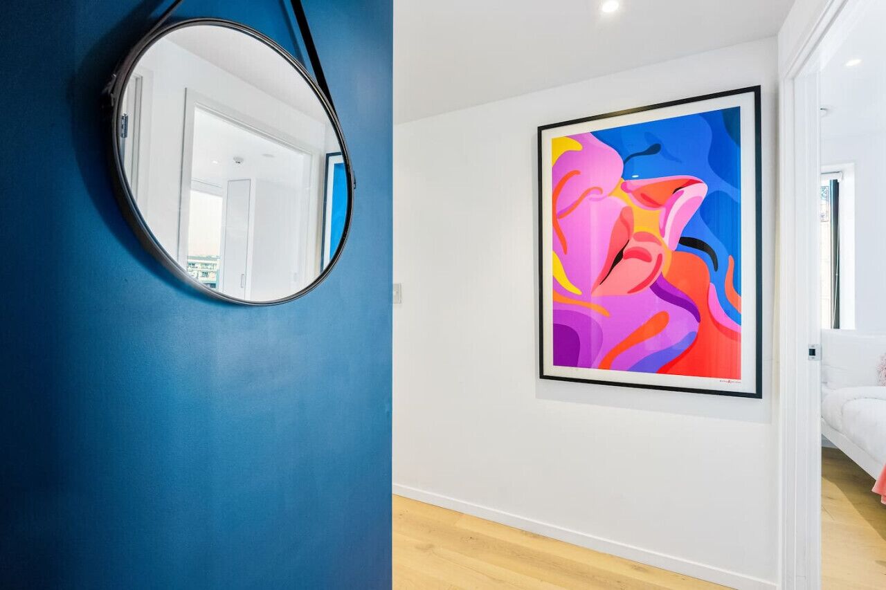 Una habitación con pared azul, un espejo redondo y un cuadro abstracto y colorido.