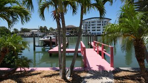 A waterfront dock with a pink walkway, palm trees, and a building in the background.