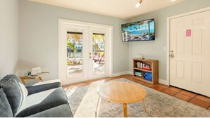 A living room with a sofa, a coffee table, a bookshelf, and a door leading to a balcony.
