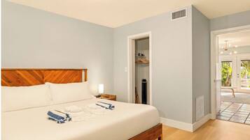A bedroom with a wooden headboard, a bed with white linens, a nightstand, and a closet with hanging clothes.
