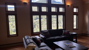 Ein geräumiges Wohnzimmer mit einem großen Bogenfenster mit Blick auf einen bewaldeten Berg.