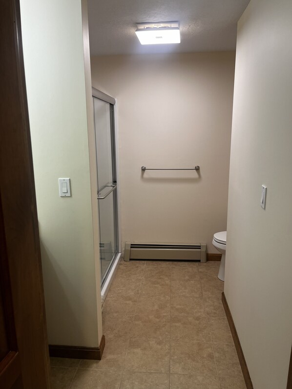 A bathroom with a glass shower door, a toilet, a towel rack, and a heater.