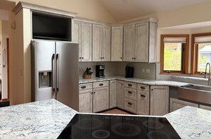 Una cocina con microondas integrado, refrigerador de acero inoxidable, gabinetes de madera, encimera de granito y cocina por inducción negra.