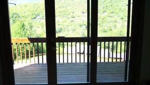 Eine Holzdielen-Terrasse mit Geländer, Blick auf einen bewaldeten Hang und einen klaren Himmel.